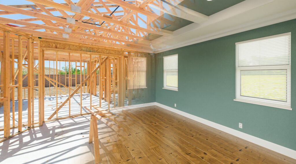 A frame of a home on the left side of the image morphing into a finish interior room with slate green walls and white trim on the right side of the image.